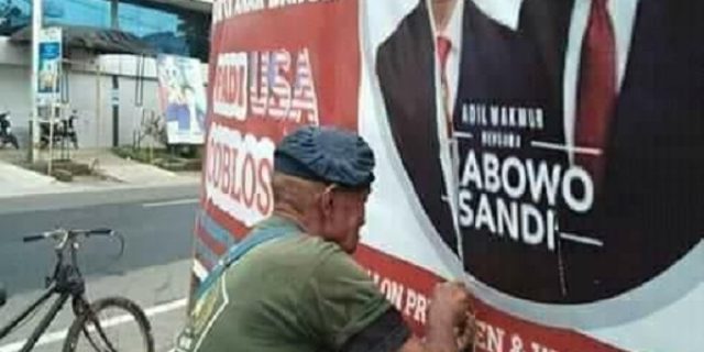 Trenyuh! Seorang Kakek Tua Menjahit Baliho Prabowo Yang Robek